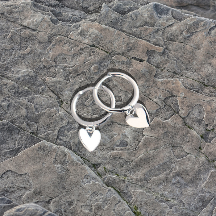 Ari Love Heart Earrings in silver on a grey stone background