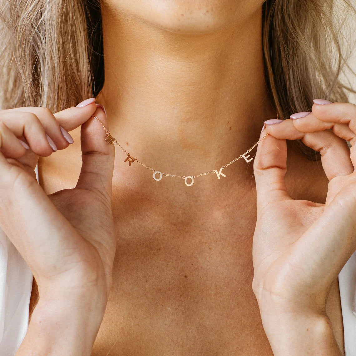 A woman holding the Amara letter necklace gold with letters B R O O K E.