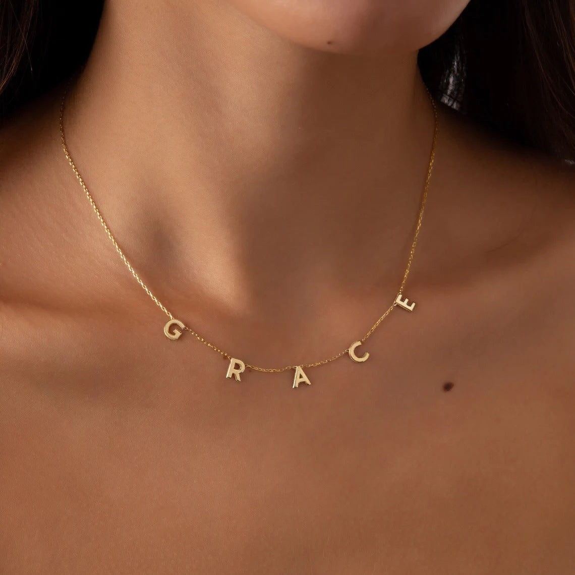 A woman wearing the Amara Initial Necklace in gold with initials G R A C E.